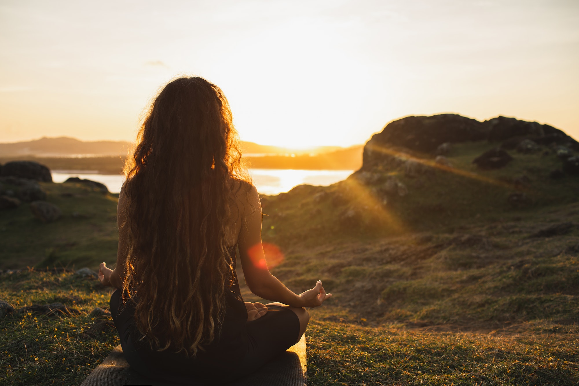 Woman meditating yoga alone at sunrise mountains. View from behind. Travel Lifestyle